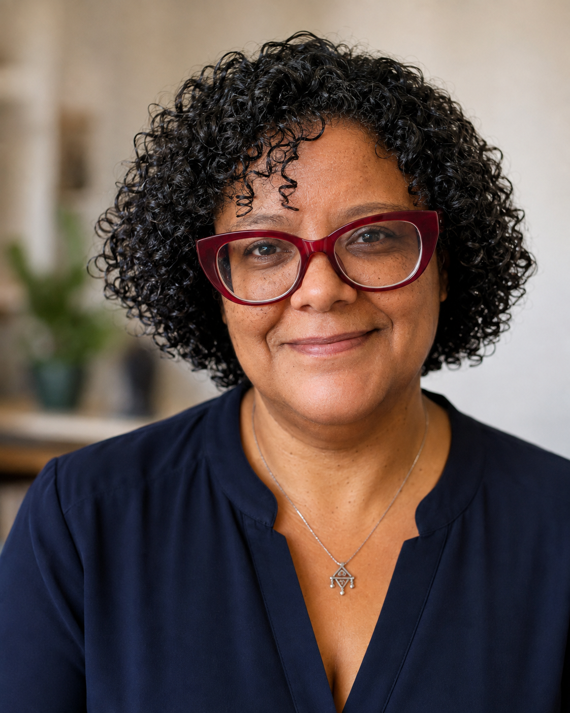 Portrait de Zakia Ouhmida : plan rapproché, lunettes à monture rouge, haut bleu marine, sur fond beige doux.